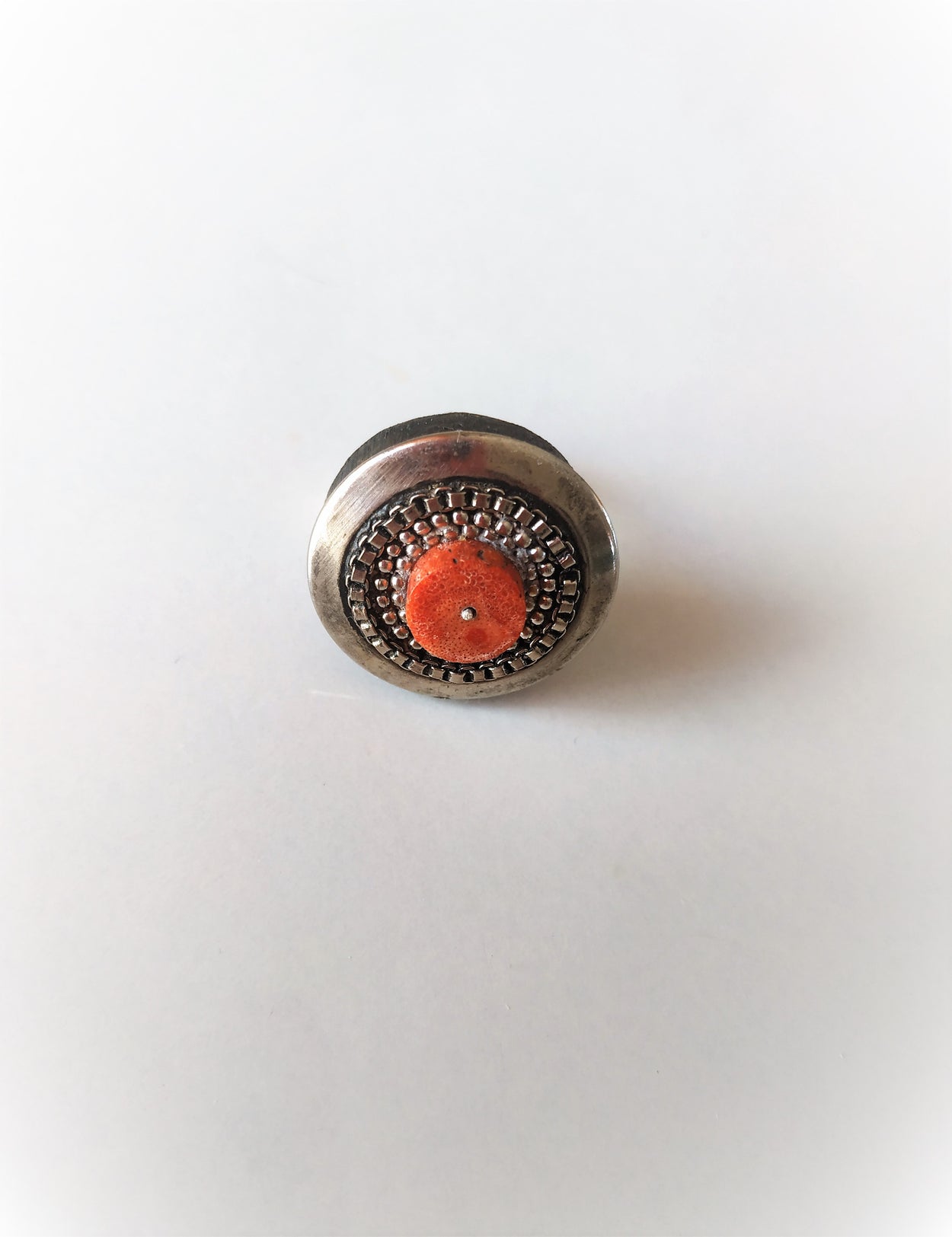 Unique white metal ring on a black platform with coral.