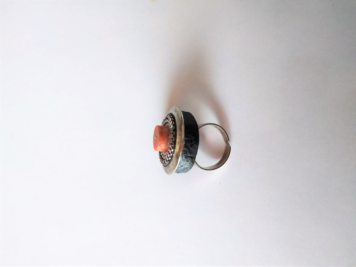Unique white metal ring on a black platform with coral.